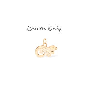 Op de afbeelding: Een goudkleurige bedel in de vorm van een gekko, met een kleine lus voor bevestiging. De gekko heeft een gekrulde staart en gestippelde details. De tekst "Charm Only" staat boven de bedel.