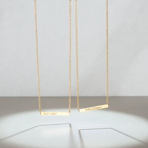 May include: Two gold necklaces with personalized bar pendants. The top pendant reads "Felix &hearts; Jasper" and the bottom pendant reads "4-27-2007".