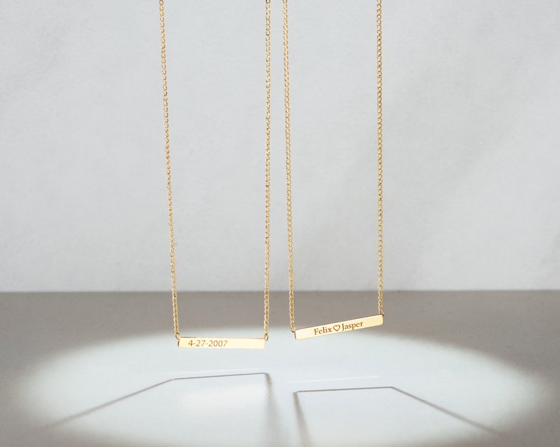 May include: Two gold necklaces with personalized bar pendants. The top pendant reads "Felix &hearts; Jasper" and the bottom pendant reads "4-27-2007".