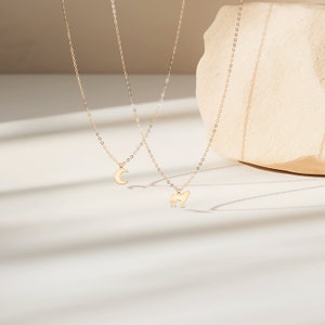 May include: Two gold necklaces with delicate chains. One necklace features a crescent moon pendant, while the other has a wolf silhouette pendant.