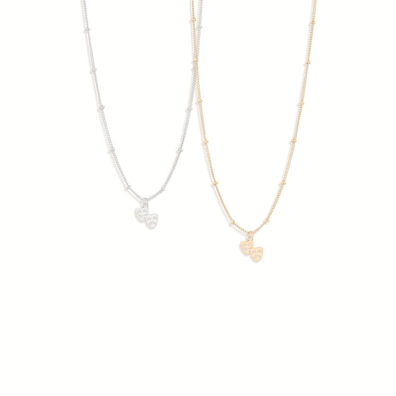 May include: Two delicate necklaces with a dainty chain and a small charm of two theater masks, one in silver and one in gold.