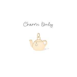 Könnte beinhalten: Ein goldfarbener Teekannen-Anhänger mit einem Teebeutel-Detail, der an einer kleinen Schlaufe hängt. Der Anhänger befindet sich vor einem weißen Hintergrund. Die Worte "Charm Only" sind in Kursivschrift über dem Anhänger geschrieben.