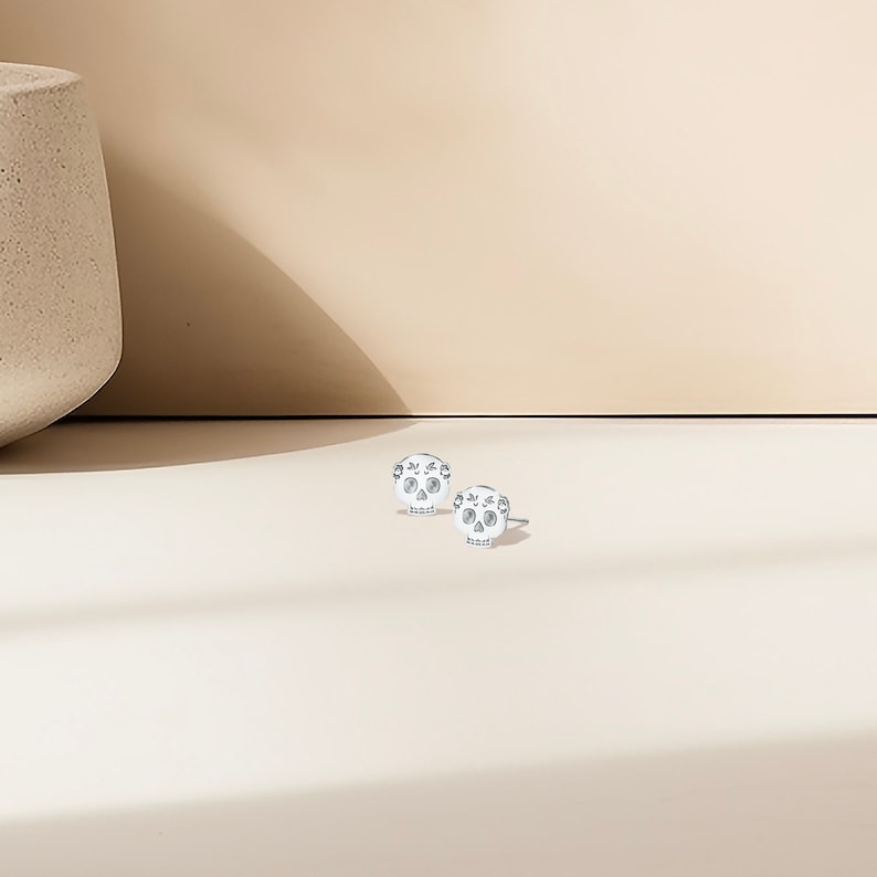 May include: A pair of silver skull stud earrings with a floral design. The earrings are small and delicate.