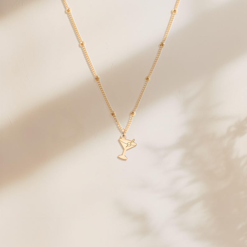 May include: A gold chain necklace with a small gold charm in the shape of a martini glass with an olive.