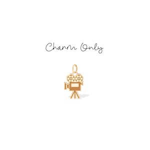 May include: A gold-colored charm in the shape of a vintage movie camera, complete with a tripod base. The charm has a loop at the top for attaching to a necklace or bracelet. The words "Charm Only" are written above the charm.