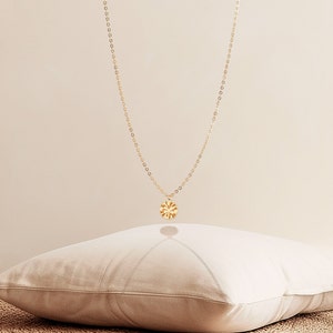 May include: A delicate gold necklace with a circular pendant featuring a sunburst design. The pendant hangs from a fine chain, creating a minimalist and elegant look. The necklace is displayed against a neutral background.