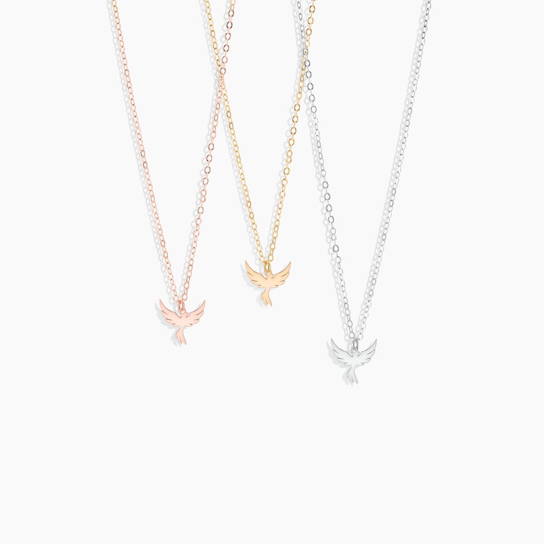 May include: Three delicate necklaces with a small bird pendant. The necklaces are available in gold, rose gold, and silver.