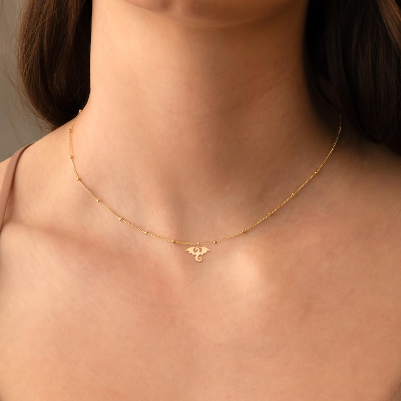 May include: A gold chain necklace with a small dragon pendant. The chain is made of tiny gold beads.