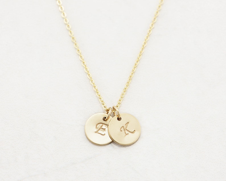 May include: A gold necklace with two small round pendants, each engraved with a letter. The letters are "E" and "K".