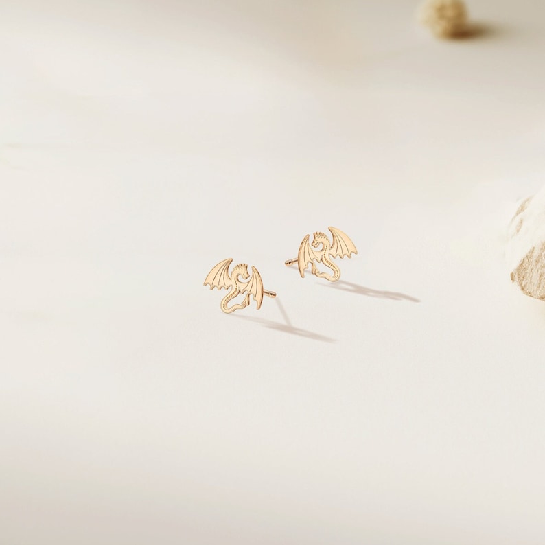 May include: A pair of gold dragon stud earrings. The earrings are small and delicate, with a detailed dragon design.