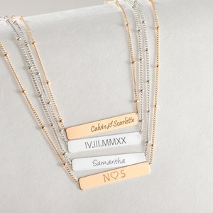 May include: Four gold bar necklaces with different engravings. The top bar reads "Calvin & Scarlette", the second bar reads "IV.III.MMXX", the third bar reads "Samantha", and the bottom bar reads "NOS" with a heart symbol.