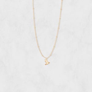May include: A delicate gold-colored necklace featuring a small bird pendant. The necklace has a fine chain with small, evenly spaced beads. The bird pendant is a simple silhouette, adding a touch of elegance to the jewelry.