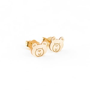 May include: A pair of gold bear-shaped stud earrings. The bears have a simple, cartoon-like design with a small nose and mouth.