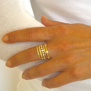 Pu&ograve; includere: Un set di cinque anelli d'oro con piccole pietre trasparenti su un dito.