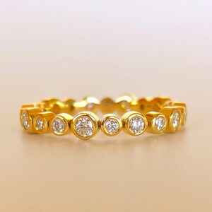 May include: A gold band ring with a row of round, bezel-set diamonds.