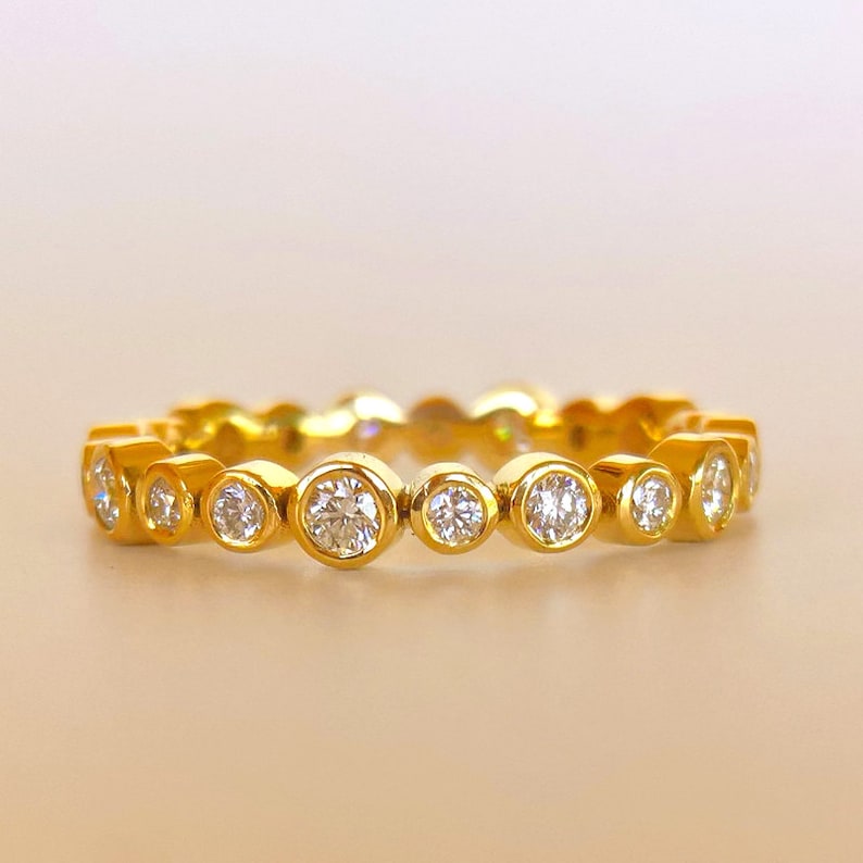 May include: A gold band ring with a row of round, bezel-set diamonds.