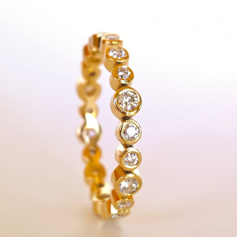 May include: A gold band ring with a row of round, bezel-set diamonds.