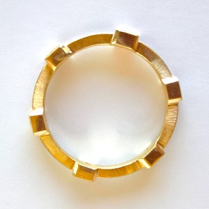 K&ouml;nnte beinhalten: Ein goldener Ring mit einer strukturierten Band und quadratischen Akzenten.