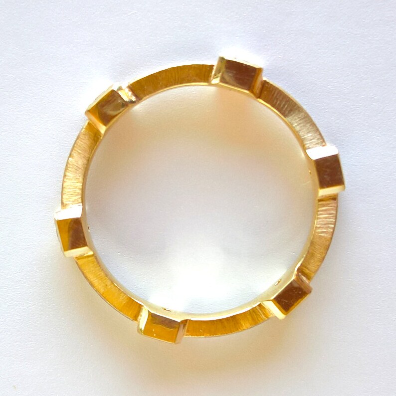 K&ouml;nnte beinhalten: Ein goldener Ring mit einer strukturierten Band und quadratischen Akzenten.