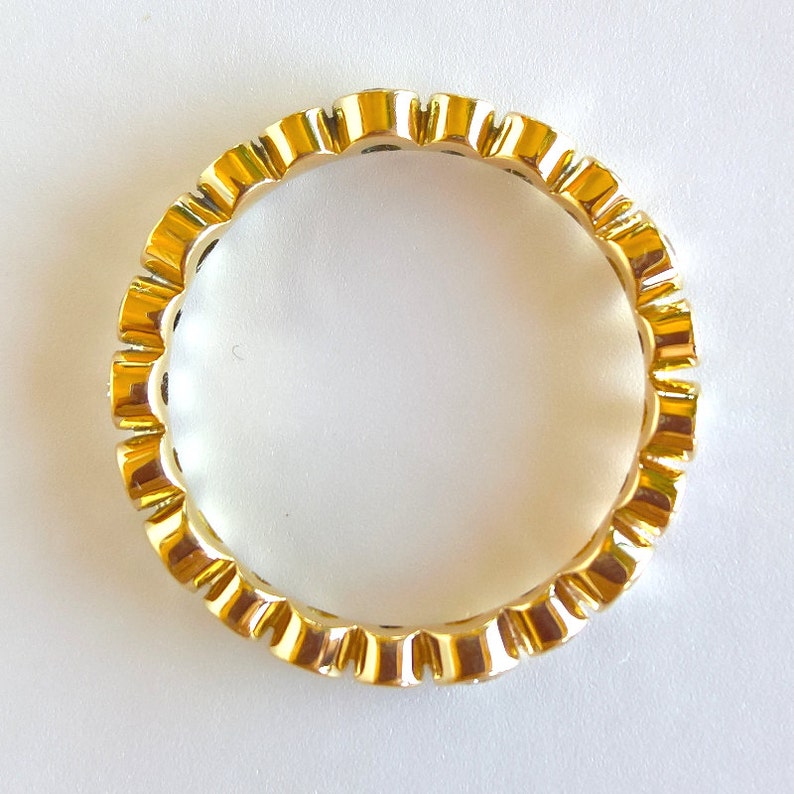 May include: A gold band ring with a scalloped edge and small clear stones set in the band.