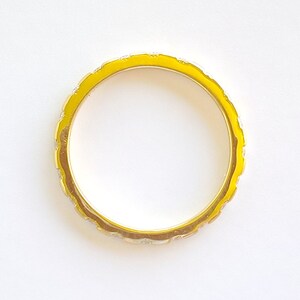 Pu&ograve; includere: Un anello d'oro con una fascia in smalto giallo e un design decorativo.