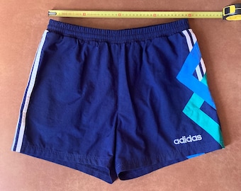 May include: Blue athletic shorts with white stripes and a geometric pattern in blue, green, and white. The shorts have the Adidas logo in white.