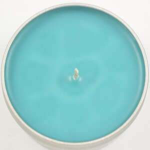 May include: A teal blue candle in a silver tin container with a white wick.