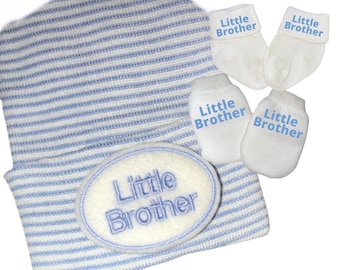 May include: A blue and white striped baby hat with a white oval patch that says "Little Brother" in blue embroidery. The set also includes two pairs of white baby socks with blue embroidery that says "Little Brother".