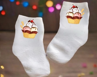 May include: A pair of white ankle socks with an ice cream cone design. The ice cream cone has three scoops of ice cream, a cherry on top, and a waffle cone.
