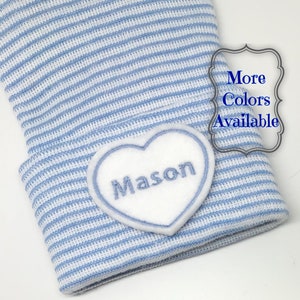May include: A blue and white striped baby hat with a white heart-shaped patch that says "Mason" on it.