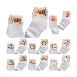 May include: White ankle socks with various autumn-themed designs. The socks feature illustrations of owls, foxes, gnomes, hedgehogs, and pumpkins. The designs incorporate fall colors like orange, brown, and yellow.