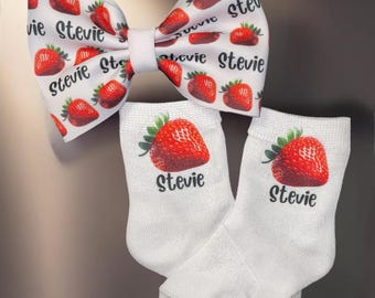 May include: White bow tie with a strawberry pattern and the name "Stevie" repeated on it. Two white socks with a single strawberry and the name "Stevie" printed on each.