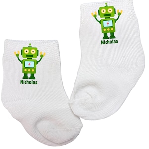 May include: Two white baby socks with a green robot graphic. The robot has a lightning bolt on its chest and the name "Nicholas" printed below. The robot has yellow arms and antennae.