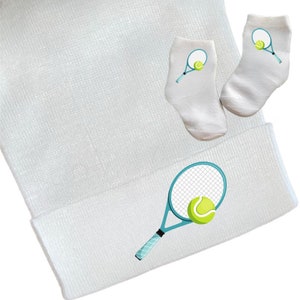 May include: White baby hat with a blue tennis racket and yellow tennis ball design. Matching white baby socks with a blue tennis racket and yellow tennis ball design.