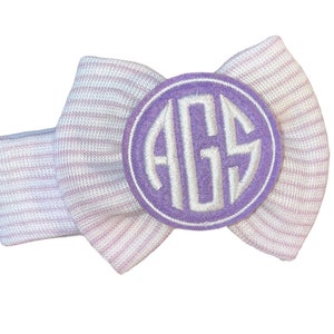 May include: A white and pink striped headband with a purple circle monogrammed with the letters "AGS".