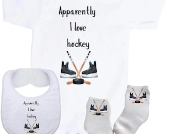May include: A white baby bodysuit, a white bib, and a pair of white socks, each featuring the text "Apparently I love hockey" in black lettering above an illustration of two crossed hockey sticks, a black puck, and two black ice skates.