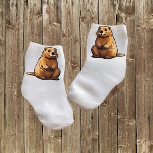Könnte beinhalten: Ein Paar weiße Knöchelsocken mit einem Cartoon-Bild eines braunen Murmeltiers auf jeder Socke.