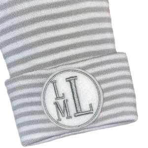 May include: Grey and white striped knitted hat with a white circle patch that has the letters "LM" embroidered in silver thread.