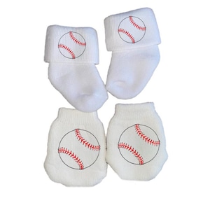 Könnte beinhalten: Set aus weißen Babysocken und -fäustlingen. Jedes Teil hat ein Baseball-Design mit roten Nähten und schwarzer Umrandung. Die Socken haben einen umgeschlagenen Bund. Das Set ist für Babys konzipiert.