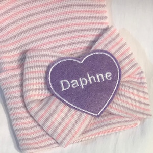 Lavender and pink stripe soft newborn hat with baby’s name i. White on lavender heart placed on bow