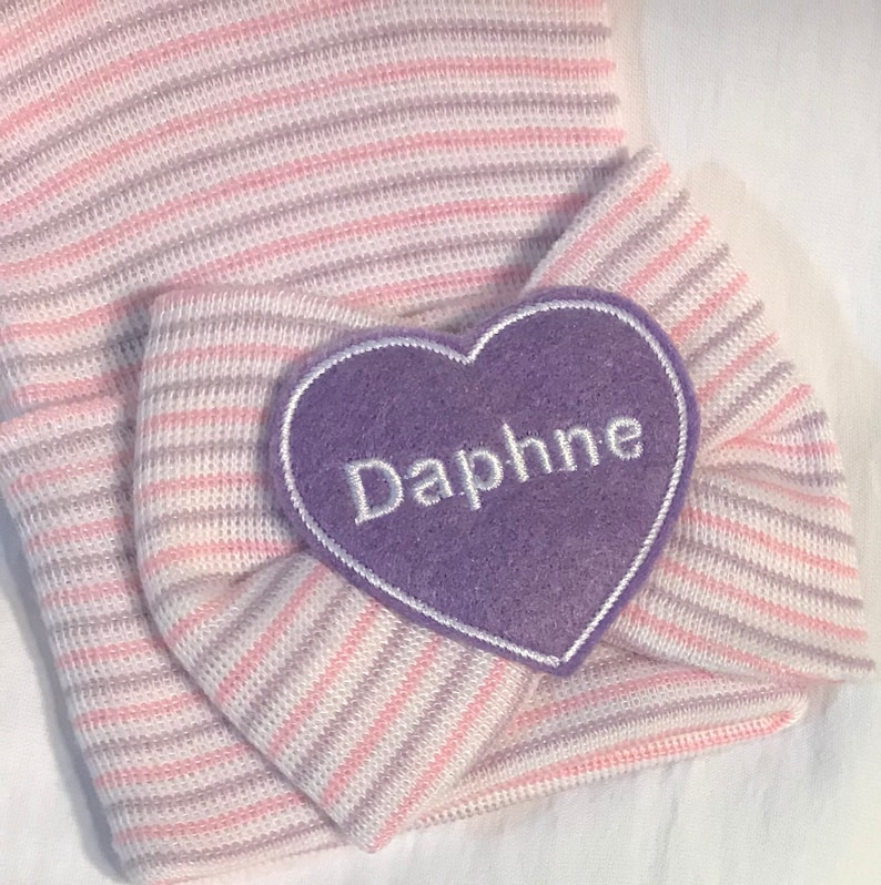 Lavender and pink stripe soft newborn hat with baby’s name i. White on lavender heart placed on bow