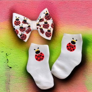 May include: A set of white socks with a ladybug design and a white bow with a ladybug design.