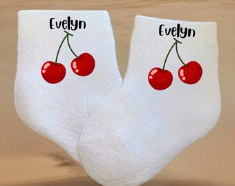 May include: A pair of white socks with red cherries and the name "Evelyn" printed on each sock.