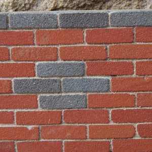May include: A brick wall with a pattern of alternating red and gray bricks. The wall is made of traditional brick and mortar.
