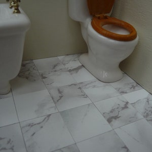 Może przedstawiać: Biała toaleta z drewnianym siedziskiem i biała wanna w łazience z podłogą z białych płytek marmurowych.