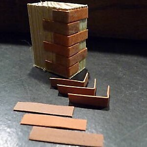 May include: A set of miniature brick corner pieces and flat bricks, made of wood and painted brown. The corner pieces are stacked in a staircase formation, and the flat bricks are arranged in a row.