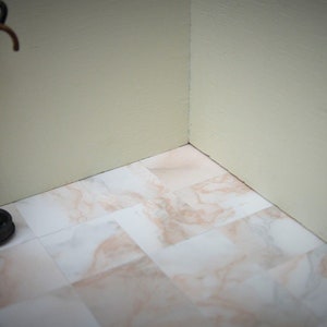 May include: A black metal umbrella stand with two umbrellas, one gray and one brown, against a white wall with a tiled floor.