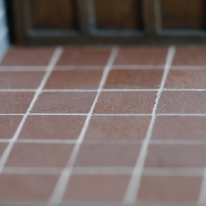 May include: A close-up of a tiled floor with brown tiles and white grout lines. The tiles are arranged in a grid pattern.