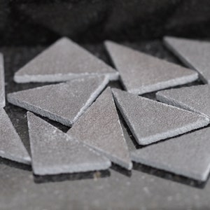 May include: A collection of grey triangular tiles arranged in a random pattern on a black surface.