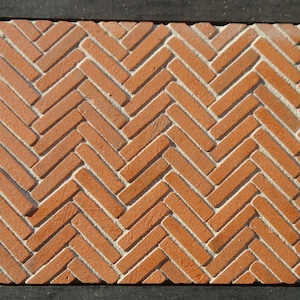 May include: A close-up of a brick floor with a herringbone pattern. The bricks are a reddish-brown color and are arranged in a staggered pattern.